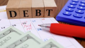 wooden blocks display the word debt, which sits on top of a calendar with the words “paid off” circled on the 16th day