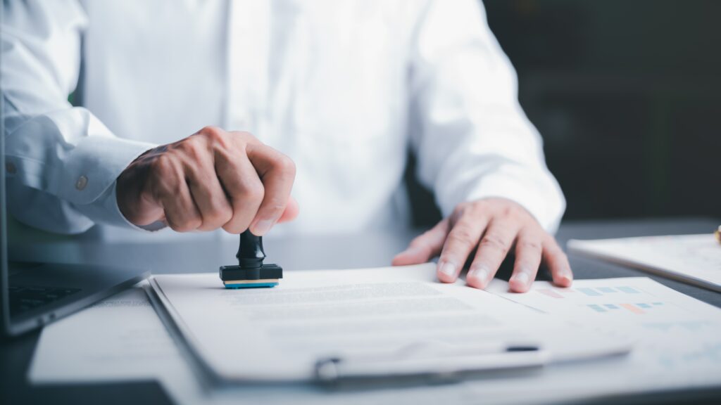 Person in white shirt marks funeral documentation with rubber stamp | Funeral financing options