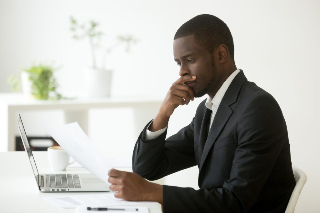Man in suit reads loan agreement and considers decision at computer desk | Funeral financing options