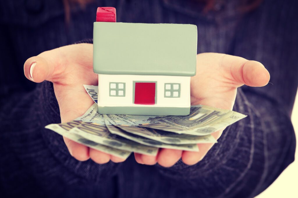 Close up of hands holding house figurine and hundred-dollar bills in palm | Relocation financing options