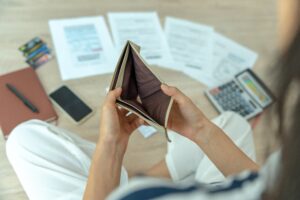 Close up of person holding open empty wallet next to unpaid bills | Best emergency loans for bad credit