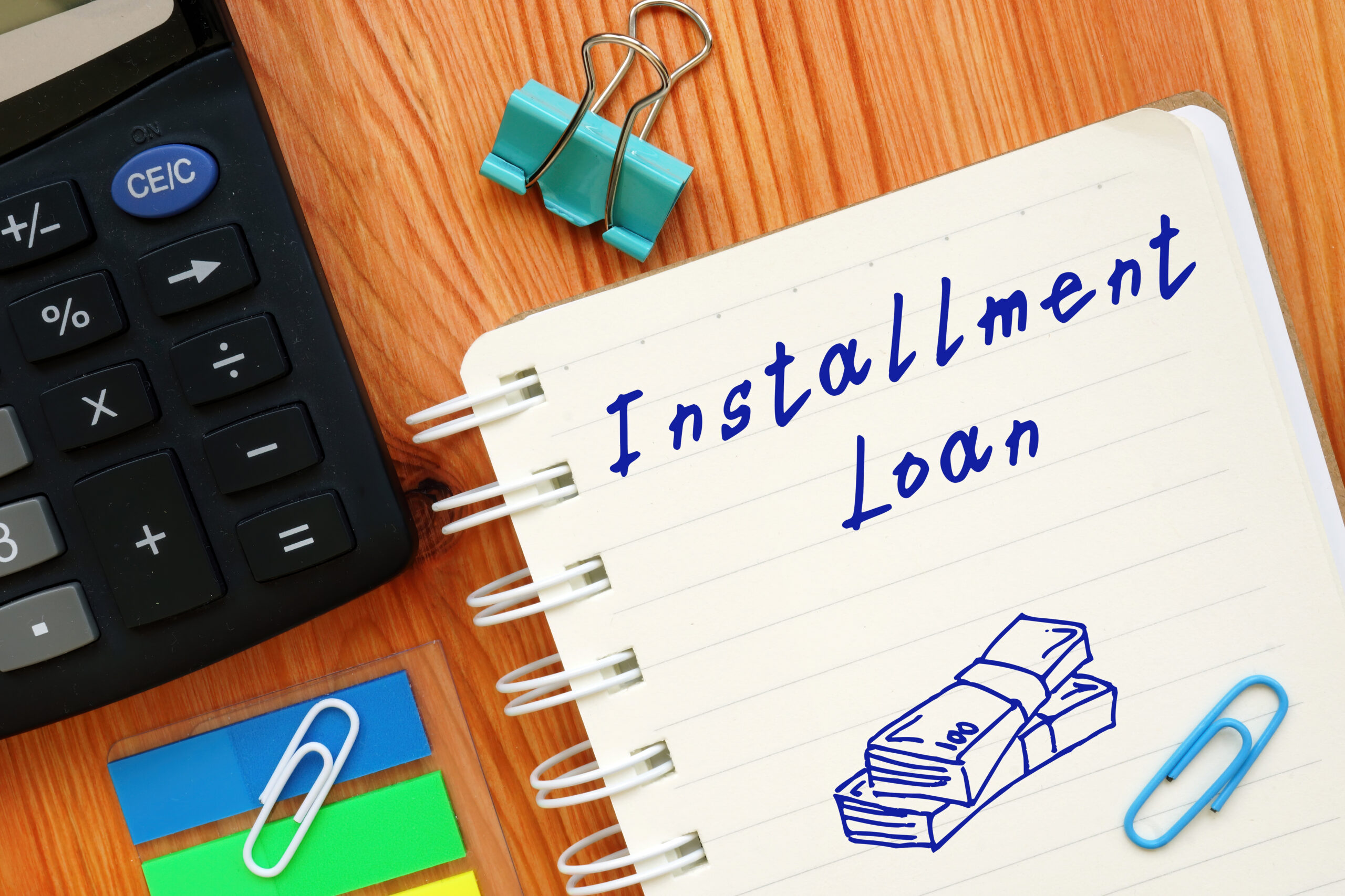 Lined paper has the phrase, “installment loans,” written in blue ink as it rests on cluttered desk | Best installment loans for bad credit
