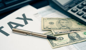 Close-up of tax documents with a pen, calculator, and US currency, including a one-dollar and five-dollar bill